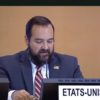 A screenshot from a video stream of the United Nation's universal periodic review of the United States. It features a man with dark hair and a dark beard, wearing a blue suit jacket and a red and white striped tie speaking into a microphone.