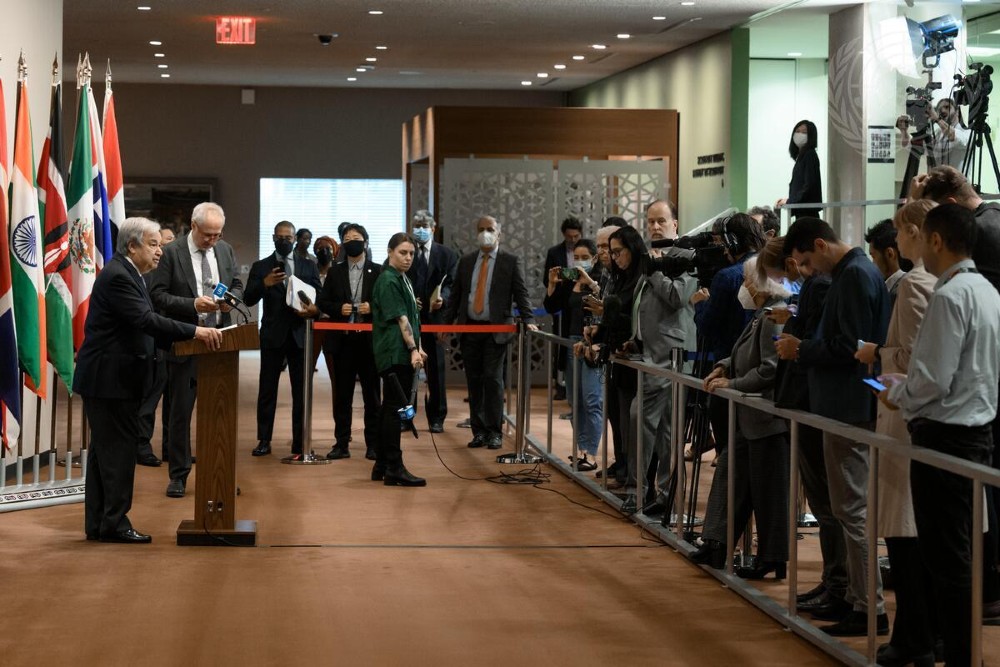 A photo of UN Secretary General Antonio Guterres standing at a podium in front of a row or reporters with cameras and microphones.